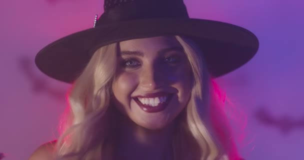 Close-up portret van gelukkig blond dame in Halloween heks kostuum glimlachen naar camera, studio schot in neon lichten — Stockvideo