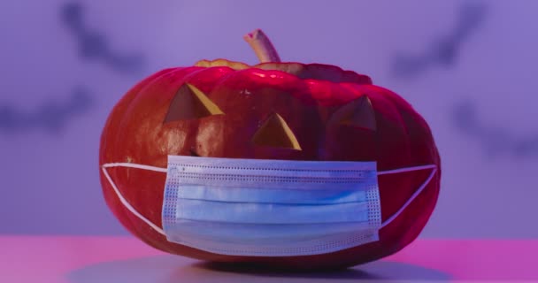 Halloween 2020. Studyjne ujęcie rzeźbionej dyni w medycznej masce ochronnej w neonach i chmurach dymu — Wideo stockowe