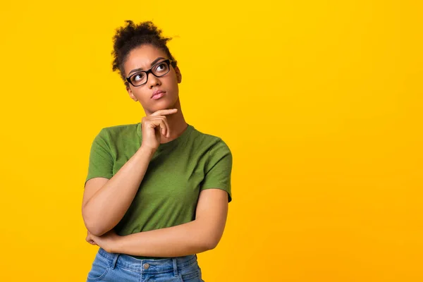 Femme noire en lunettes réfléchissant à la question, toucher le menton — Photo