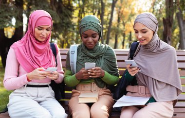 Dışarıda oturan Üç Müslüman Kadın Cep Telefonu Mesajı Kullanıyor