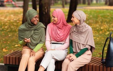 Üç Müslüman kadın dışarıda bankta oturmuş konuşuyor.
