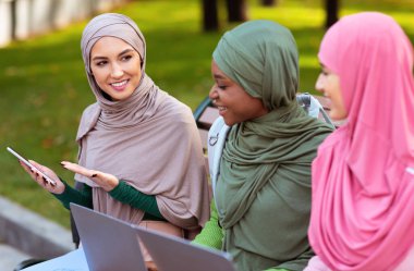 Açık havada oturan Arkadaşlara Akıllı Telefon Uygulaması Öneren Müslüman Kadın