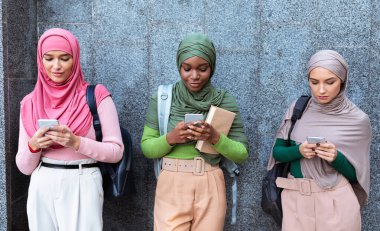 Gri Duvar Üzerinde Duran Cep Telefonu Kullanan Üç Modern Müslüman Kadın