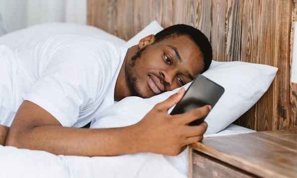 Frustrado africano chico mirando móvil acostado en la cama — Foto de Stock