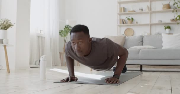 Motiverad afrikansk amerikan som tränar armhävningar på golvet hemma — Stockvideo
