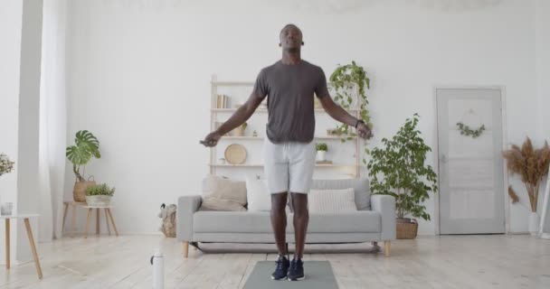 Aktiv svart idrottsman utför konditionsträning med hopprep, utövar i vardagsrummet hemma — Stockvideo