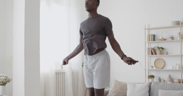 Καρδιο προπόνηση στο σπίτι. Νεαρός Αφροαμερικάνος πηδάει με σχοινάκι — Αρχείο Βίντεο