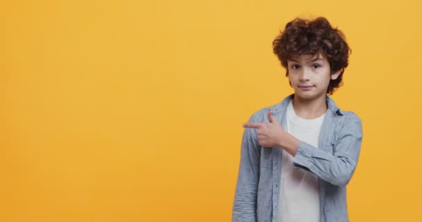 Regarde là. mignon bouclé garçon pointant avec doigt à vide espace et hochant la tête, orange fond studio — Video