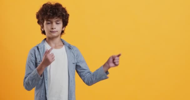 Cool offer. Little boy showing aside with both hands, pointing at copy space , orange background — Stock Video