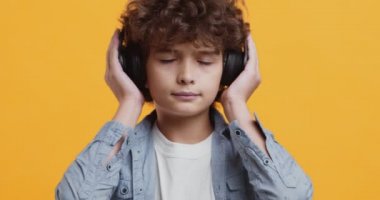 Büyük kablosuz kulaklıklarla müzik dinleyen kıvırcık çocuk portresini kapat.
