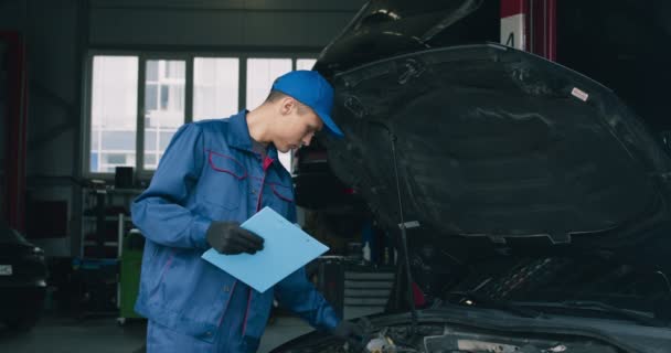 Концепция автострахования. Механический инспектор исследует повреждения на транспортном средстве и записывает его в блокнот при обслуживании — стоковое видео