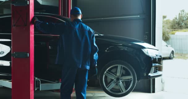 Vehículo de elevación del trabajador de servicio de automóviles en polipasto antes del mantenimiento en taller de servicio — Vídeos de Stock