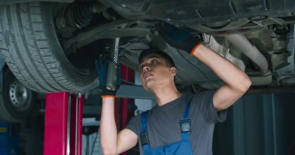 Νεαρός μηχανικός επισκευή ανάρτησης αυτοκινήτου, στέκεται κάτω από το όχημα στο γκαράζ — Αρχείο Βίντεο
