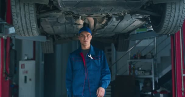 Vidám magabiztos szerelő mosolyog a kamerába, találkozás ügyfelekkel bejáratánál autó karbantartás műhely — Stock videók