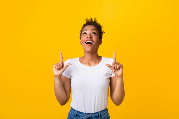 Gelukkig afro vrouw wijzend vingers omhoog naar kopieerruimte — Stockfoto