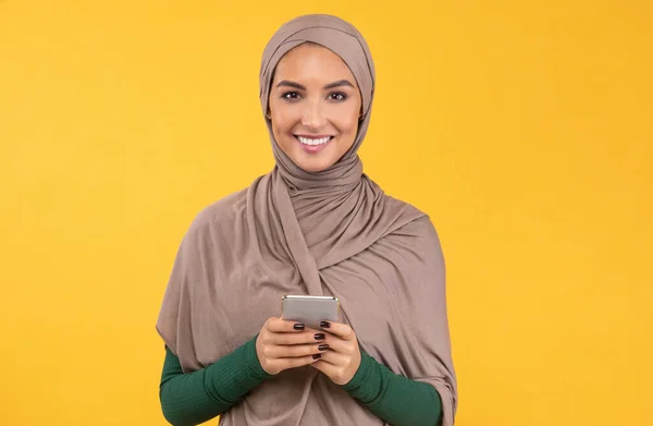 Wanita Muslim muda menggunakan Smartphone berdiri di atas Latar Belakang Studio Kuning — Stok Foto