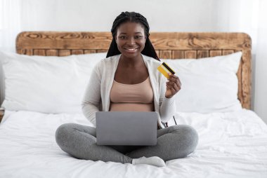 Kolay ödemeler. Siyah Hamile Kadın Evde Dizüstü bilgisayar ve kredi kartı kullanıyor