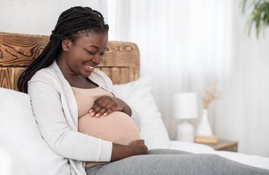 Bebeği bekliyorum. Hamile Afrikalı Kadın Şefkatle Sarılıyor, Yatakta Rahatlıyor
