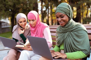 Diz üstü bilgisayar ve kitaplarla Öğrenen Üç Modern Arap Kadın