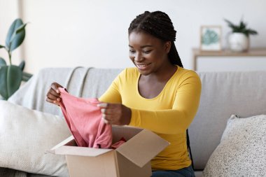 Teslimat servisi. Heyecanlı Afrikalı Kadın Paket Kutusunu Evde Satın Alma ile Boşaltıyor