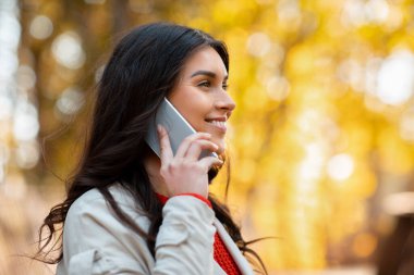 Parlak güneşli bir günde, Autumn Park 'ta cep telefonuyla konuşan genç bir bayan. Anlaşıldı.