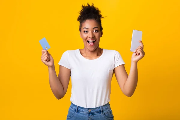 Excitada senhora negra segurando cartão de crédito e celular no estúdio — Fotografia de Stock