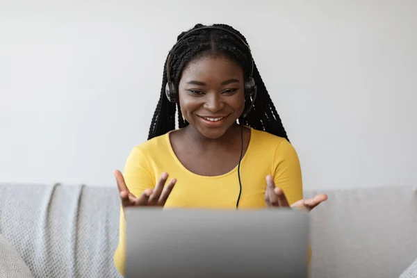 Telekonferans. Kulaklık takmış neşeli genç siyahi kadın dizüstü bilgisayarında video çağrısı yapıyor. — Stok fotoğraf