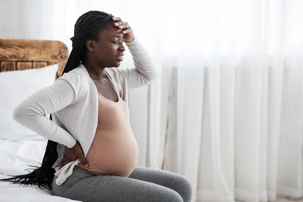 Sjuk afrikansk gravid kvinna mår dåligt hemma, sitter på sängen — Stockfoto