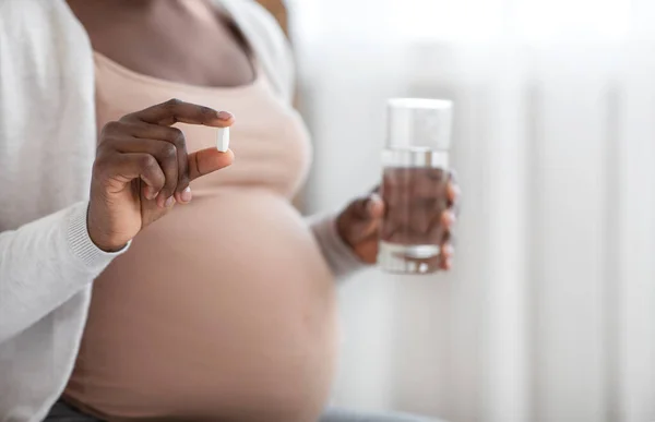 Συμπληρώματα κατά τη διάρκεια της εγκυμοσύνης. Αγνώριστη μαύρη προσδοκώμενη κυρία κρατώντας χάπι και γυαλί νερού — Φωτογραφία Αρχείου