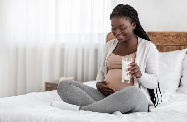 Calcio saludable. Mujer embarazada negra con vaso de leche sentada en la cama — Foto de Stock