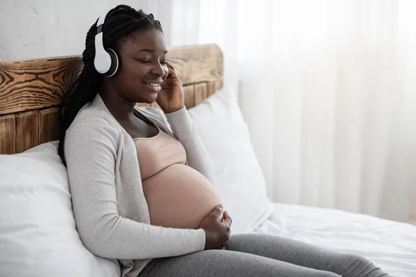 Embarazo Ocio. Calma mujer embarazada negro escuchar música en los auriculares en casa — Foto de Stock