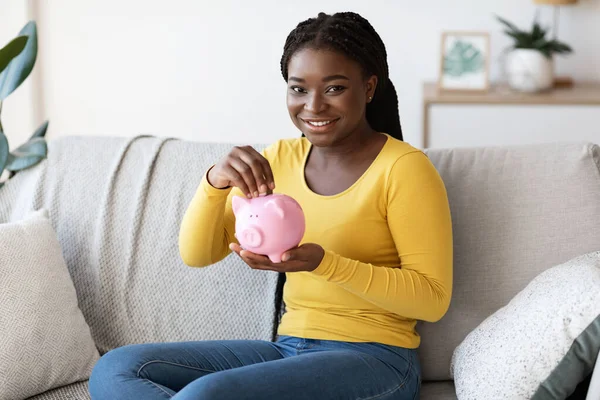 Gelukkig Afro-Amerikaanse vrouw Holding Piggy Bank, zitten op de bank thuis — Stockfoto