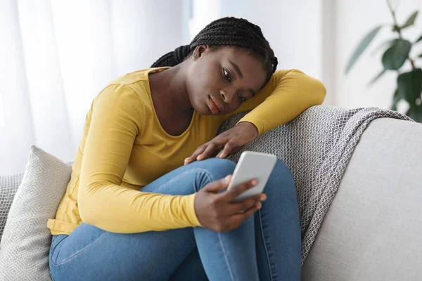 Mulher Africano perturbado sentado no sofá com Smartphone, sentindo-se sozinho e deprimido — Fotografia de Stock