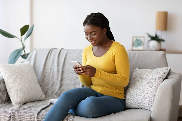 Young african american woman spending time with smartphone at home, browsing internet — Stock Photo, Image