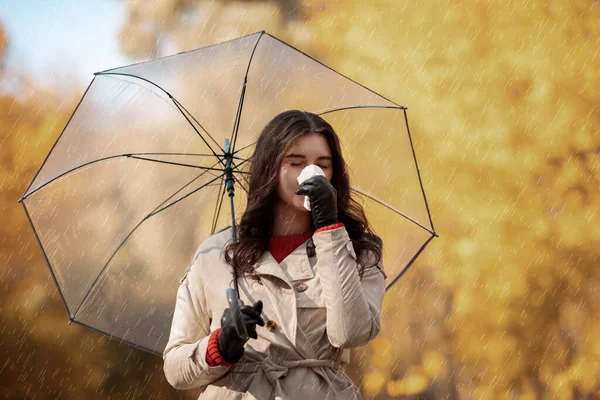 Schöne junge Frau mit Schirm, die Erkältung oder Grippe hat, am Herbsttag draußen in Serviette niest, Kopierraum — Stockfoto