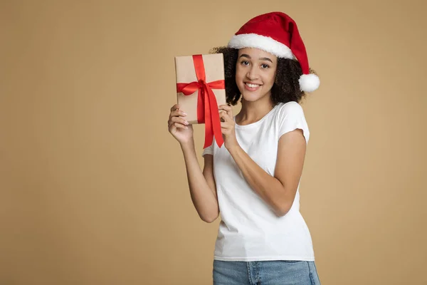 Mujer afroamericana milenaria en sombrero de Santa Claus muestra caja con regalo para Año Nuevo o Navidad — Foto de Stock