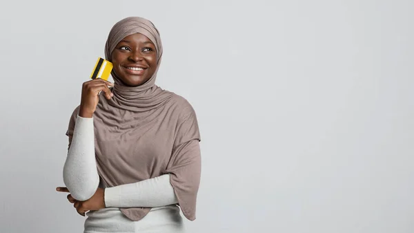 Pensive Αφρικανή μουσουλμάνα γυναίκα σε hijab κρατώντας πιστωτική κάρτα και κοιτάζοντας μακριά — Φωτογραφία Αρχείου