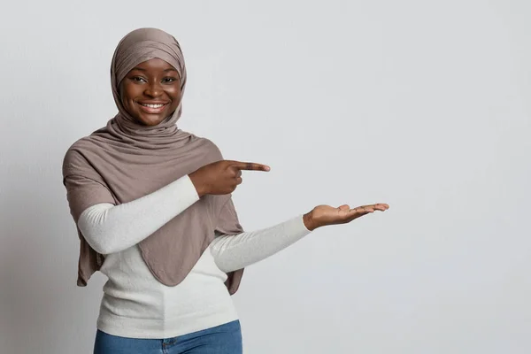Χαμογελαστή μαύρη μουσουλμάνα κυρία με χιτζάμπ που δείχνει με το δάχτυλο την ανοιχτή παλάμη της — Φωτογραφία Αρχείου