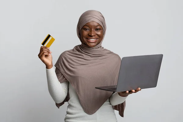 Інтернет-магазини. Чорна ісламська жінка в хіджабі тримає ноутбук і кредитну картку — стокове фото