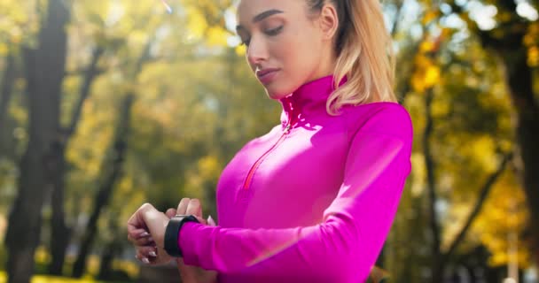 Millennial ξανθιά ενεργοποίηση λειτουργία κατάρτισης για SmartWatch, προετοιμασία για τρέξιμο προπόνηση στο πάρκο φθινόπωρο — Αρχείο Βίντεο
