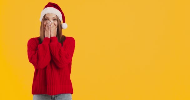 Jovem mulher em camisola de malha vermelha e chapéu de Natal de Santa apontando os dedos para o espaço de cópia, fundo laranja — Vídeo de Stock