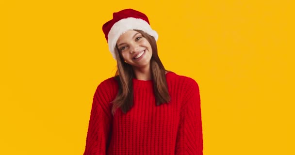 Adorabile giovane donna in cappello di Natale Santa e maglione rosso a maglia sorridente alla fotocamera su sfondo arancione — Video Stock