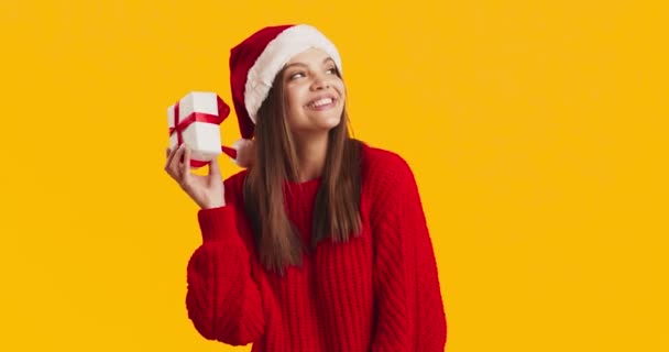 Retrato joven mujer curiosa en sombrero de santa sacudiendo regalo de Navidad, escuchando lo que traquetea en caja de regalo — Vídeos de Stock