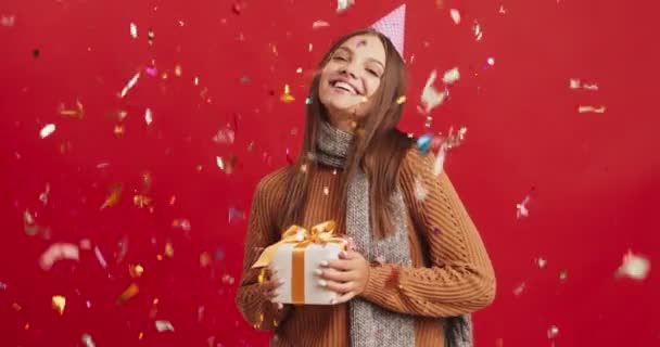 Confetti padající na vzrušenou mladou ženu s legrační party kužel na hlavě drží dárek box a přijímá pozdravy — Stock video