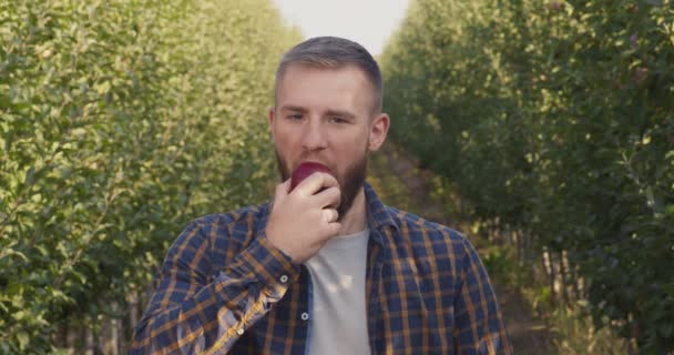 Retrato ao ar livre de jovem mordendo maçã fresca, desfrutando de sabor natural no jardim — Vídeo de Stock