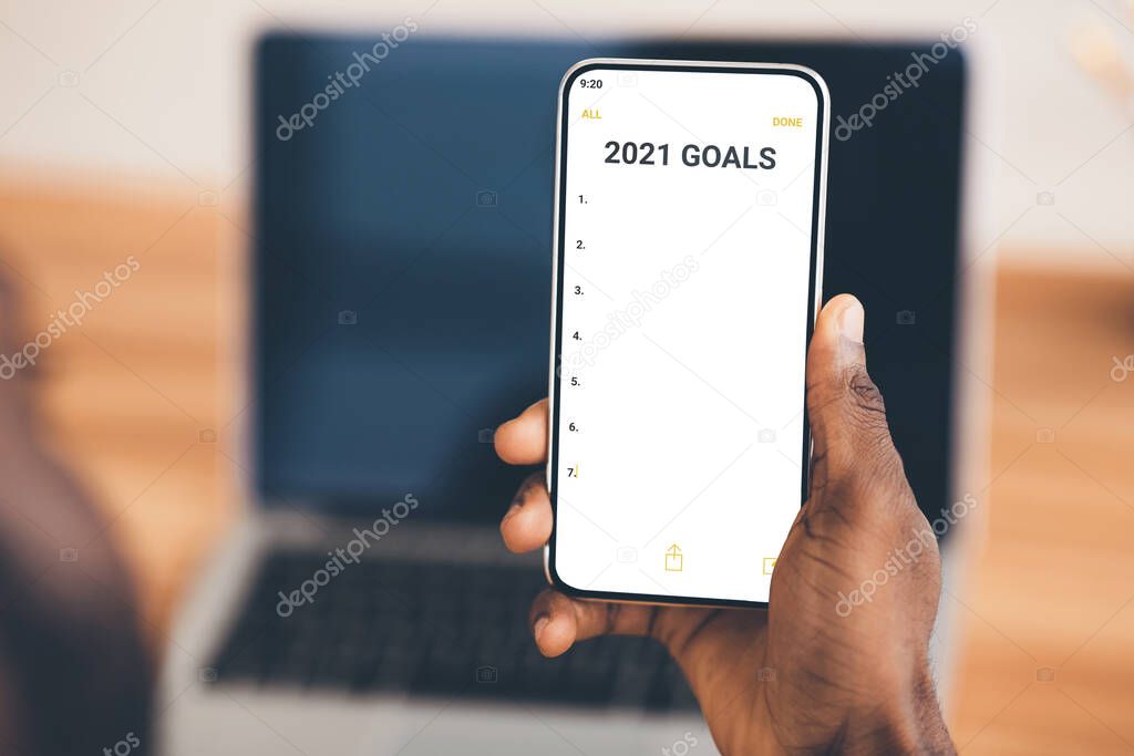 Black Businessman Holding Smartphone With 2021 Goals Checklist Sitting Indoors, Cropped