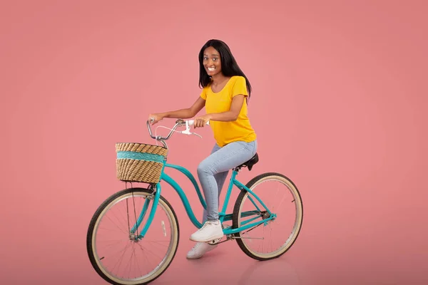 Full length portrait of beautiful African American woman riding vintage bicycle over pink studio background — Stock Photo, Image
