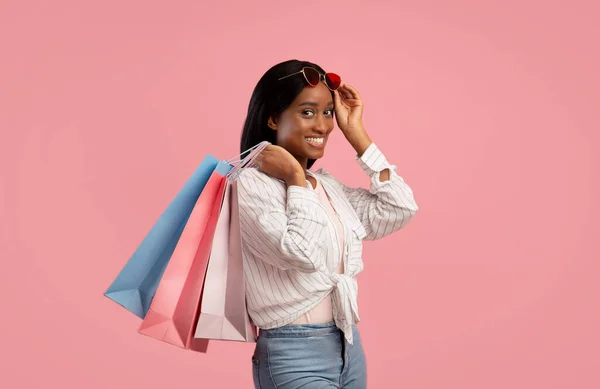 Preciosa mujer joven con bolsas de compras sonriendo y mirando a la cámara en el fondo del estudio rosa —  Fotos de Stock