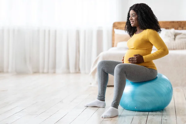 Femme enceinte afro-américaine souriante assise sur une balle de fitness — Photo