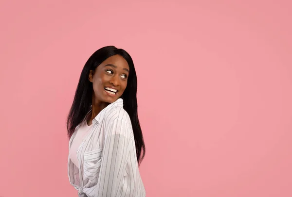 Verspielte schwarze Frau blickt hinter ihrer Schulter auf leeren Raum auf rosa Studiohintergrund — Stockfoto